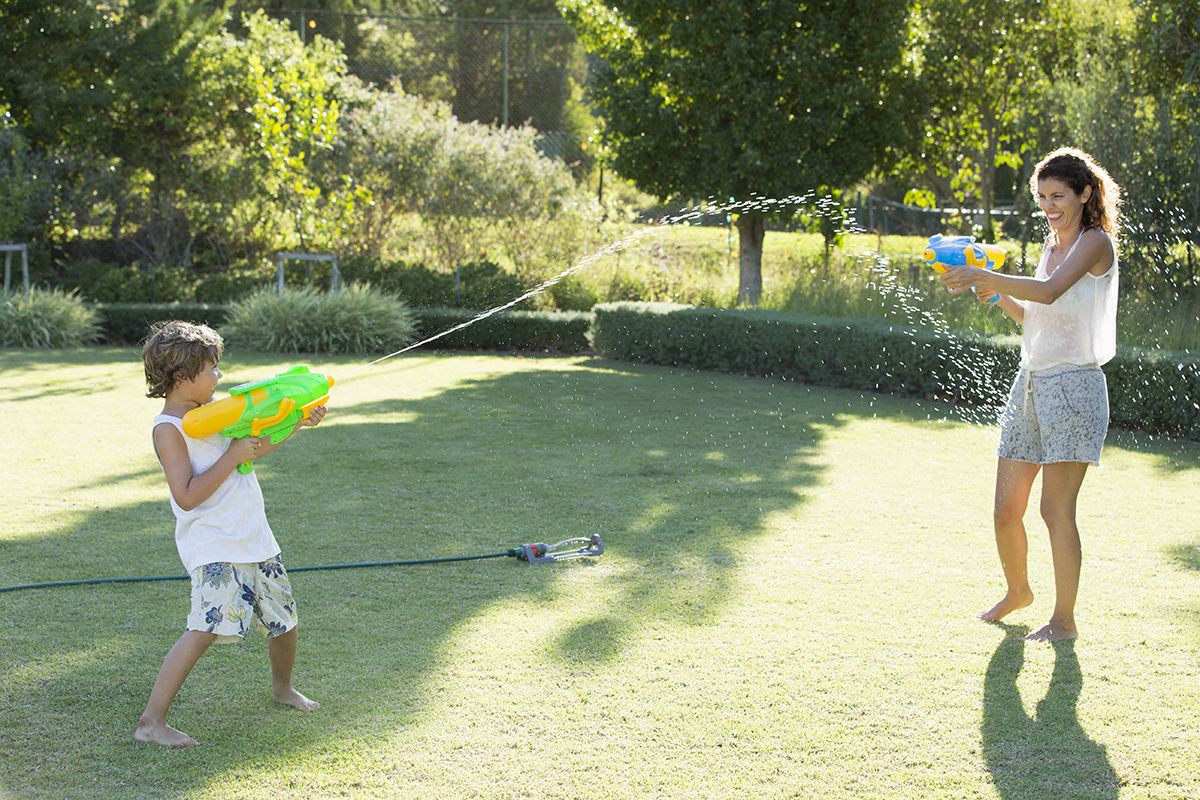 Playful mother and son with squirt guns in sunny summer backyard ...